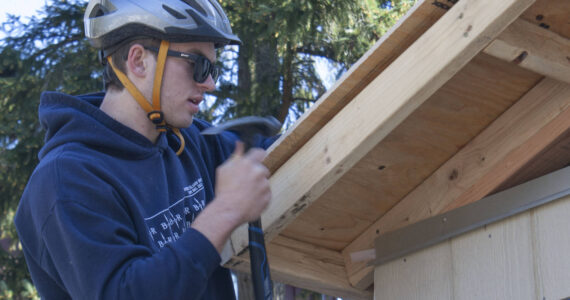 Student James Phillips secures a piece of plywood to the roof of the Hyla students’ tiny home project.